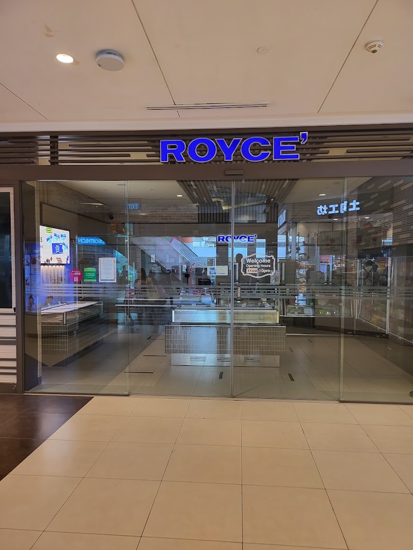 The glass storefront of Royce' chocolate shop, featuring its illuminated blue sign and inviting entrance.