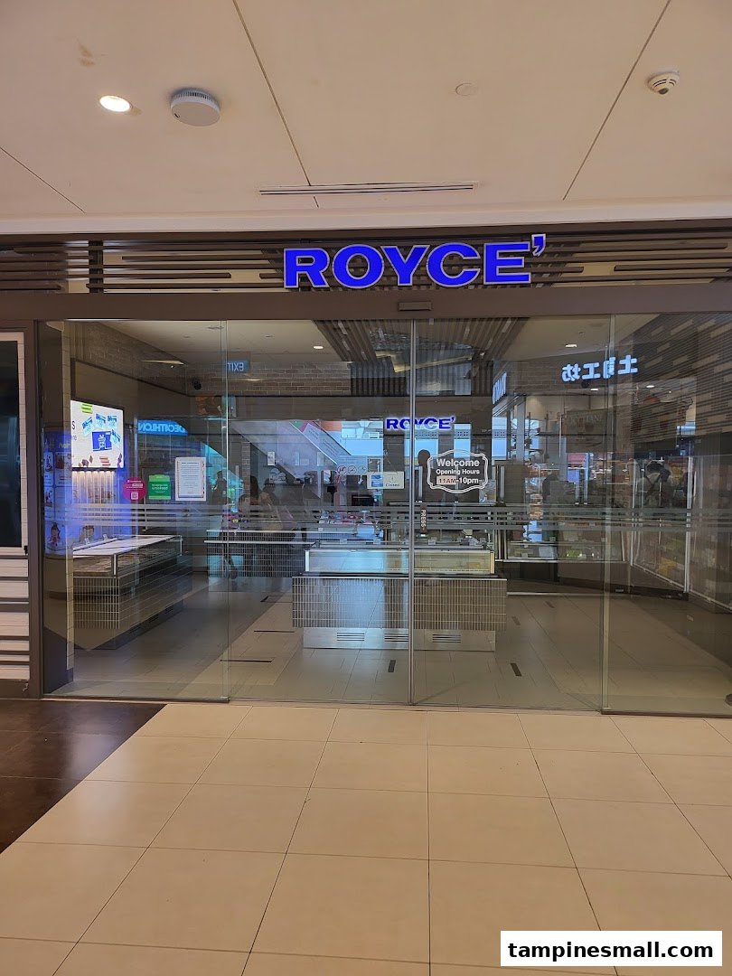 The glass storefront of Royce' chocolate shop, featuring its illuminated blue sign and inviting entrance.