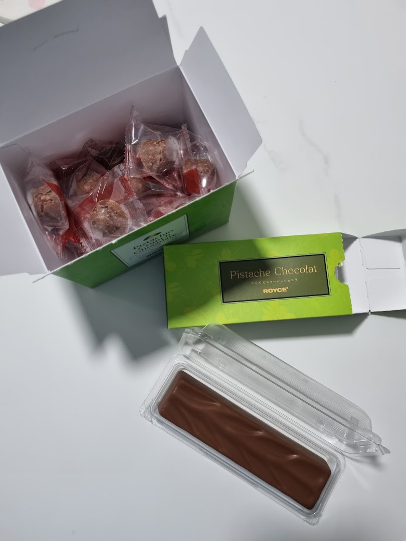 An open box of individually wrapped chocolates and a bar of Royce's Pistache Chocolat.