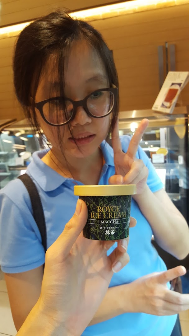 A person holds a Royce Maccha Ice Cream cup, with another person making a peace sign in the background.