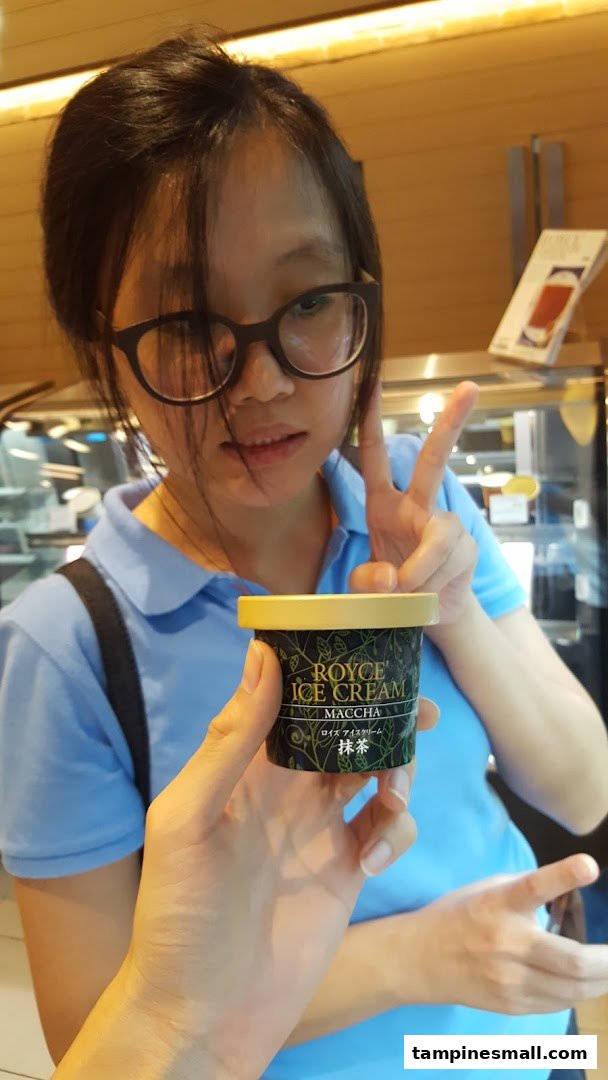 A person holds a Royce Maccha Ice Cream cup, with another person making a peace sign in the background.