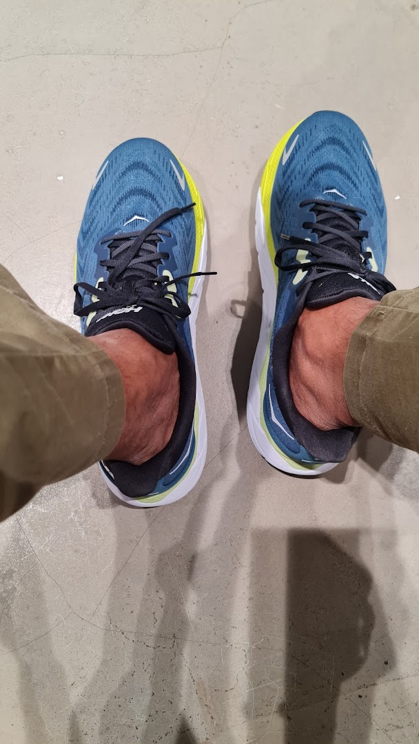 A person's feet wearing blue and yellow running shoes on a concrete floor, likely inside the shop.