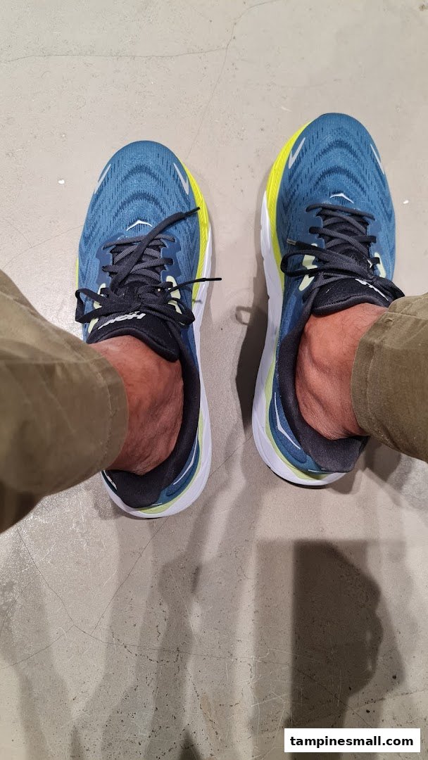 A person's feet wearing blue and yellow running shoes on a concrete floor, likely inside the shop.