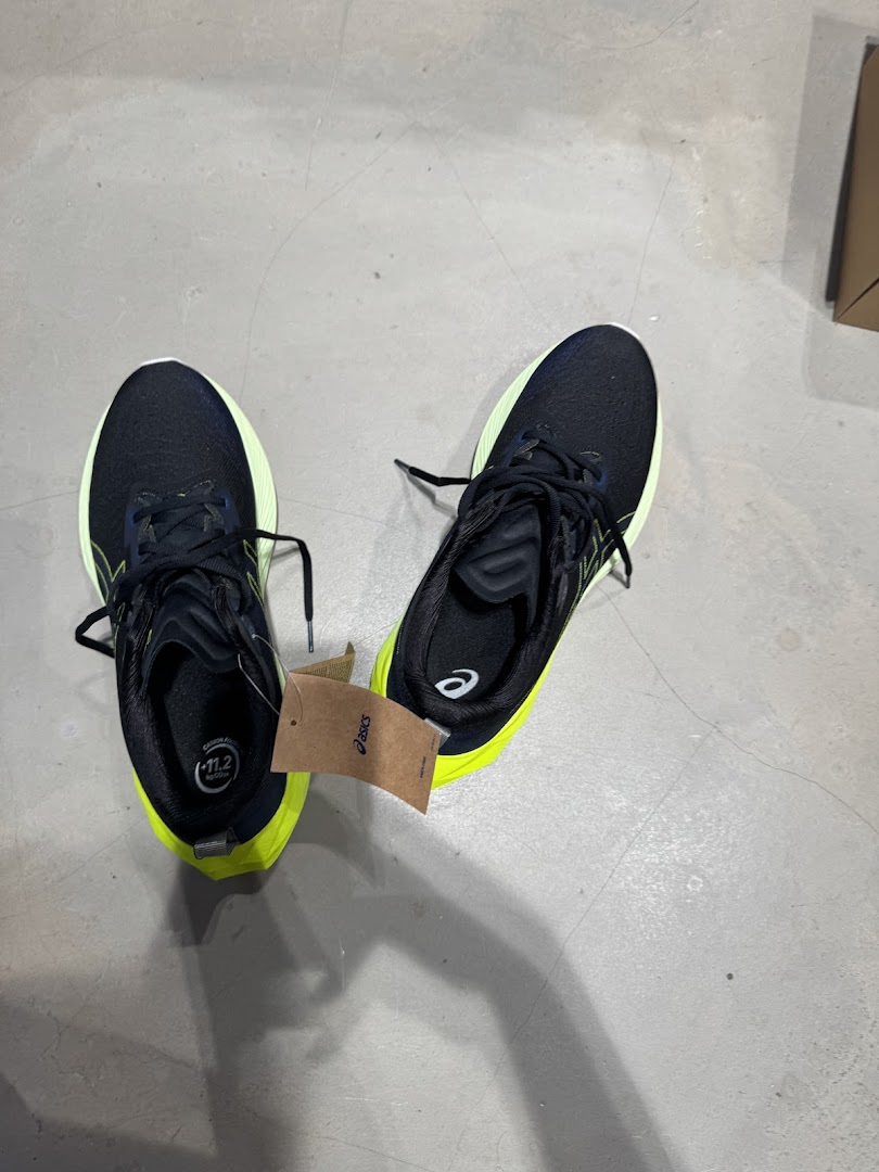 A pair of black and neon yellow running shoes with an ASICS tag on a concrete floor.