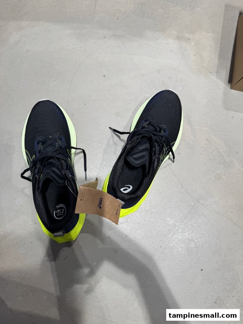 A pair of black and neon yellow running shoes with an ASICS tag on a concrete floor.