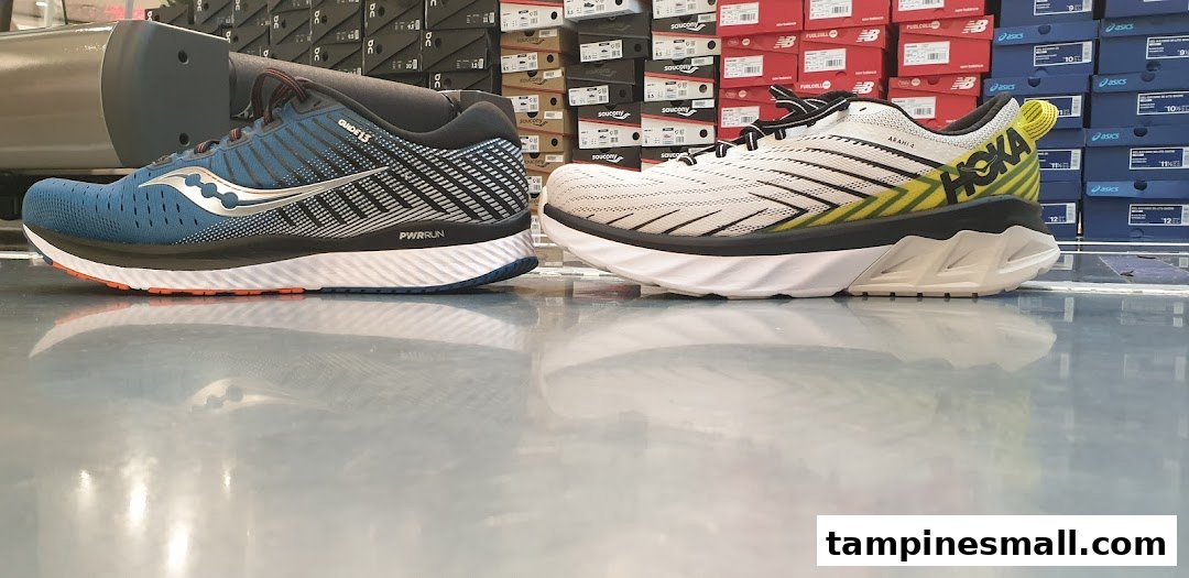 Two running shoes, a blue Saucony and a white Hoka, displayed on a reflective floor inside a shoe store.