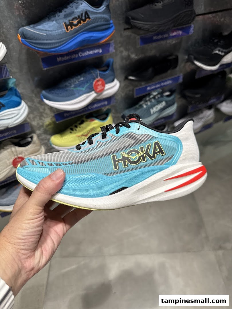 A hand holds a light blue Hoka running shoe inside Running Lab, with other shoes displayed.