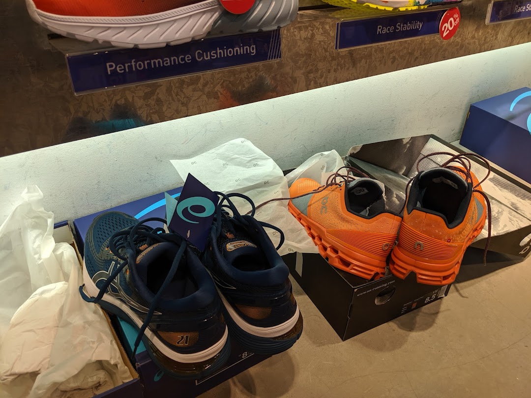 Two pairs of running shoes, blue and orange, displayed with product feature signs.