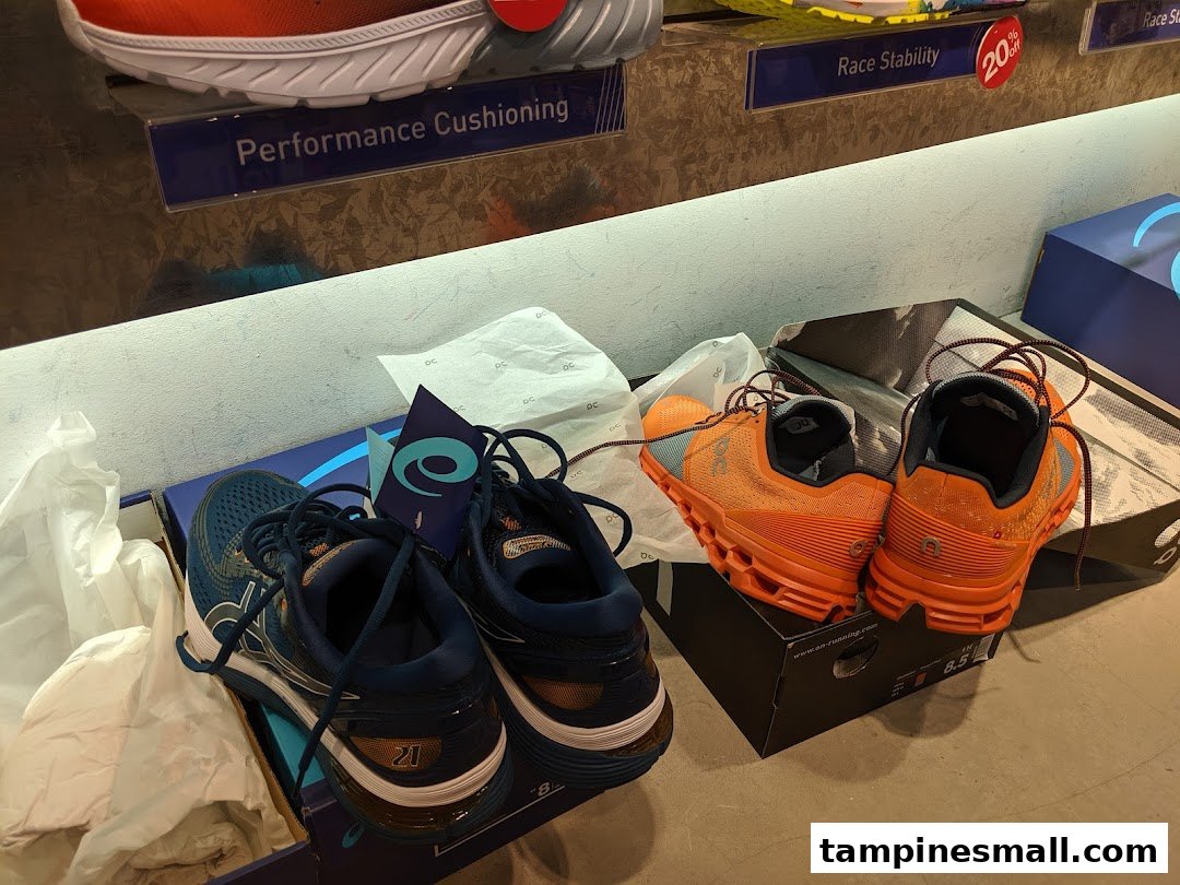 Two pairs of running shoes, blue and orange, displayed with product feature signs.