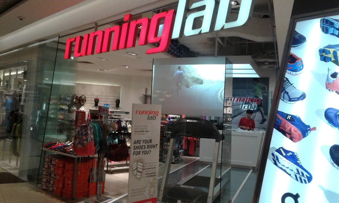 The storefront of Running Lab, showcasing its illuminated signage, display shoes, and a treadmill for gait analysis.