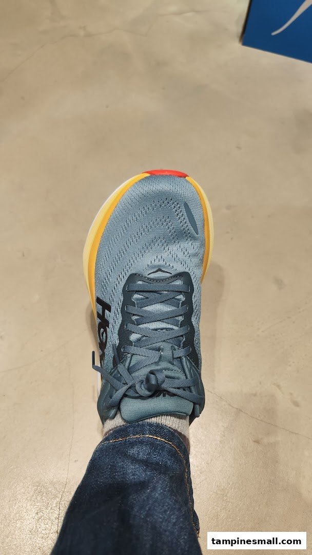 A person's foot wearing a blue Hoka running shoe on a shop floor, showcasing footwear.