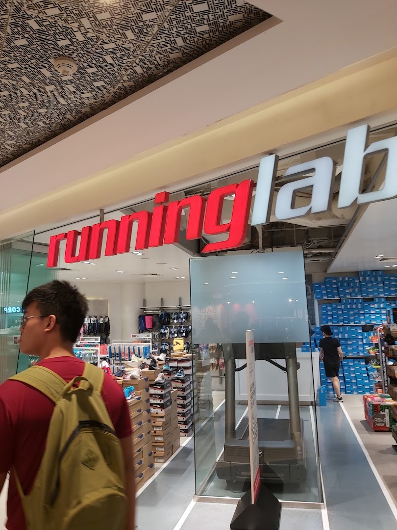 A person walks past the glass storefront of Running Lab, showcasing athletic footwear and a treadmill inside.