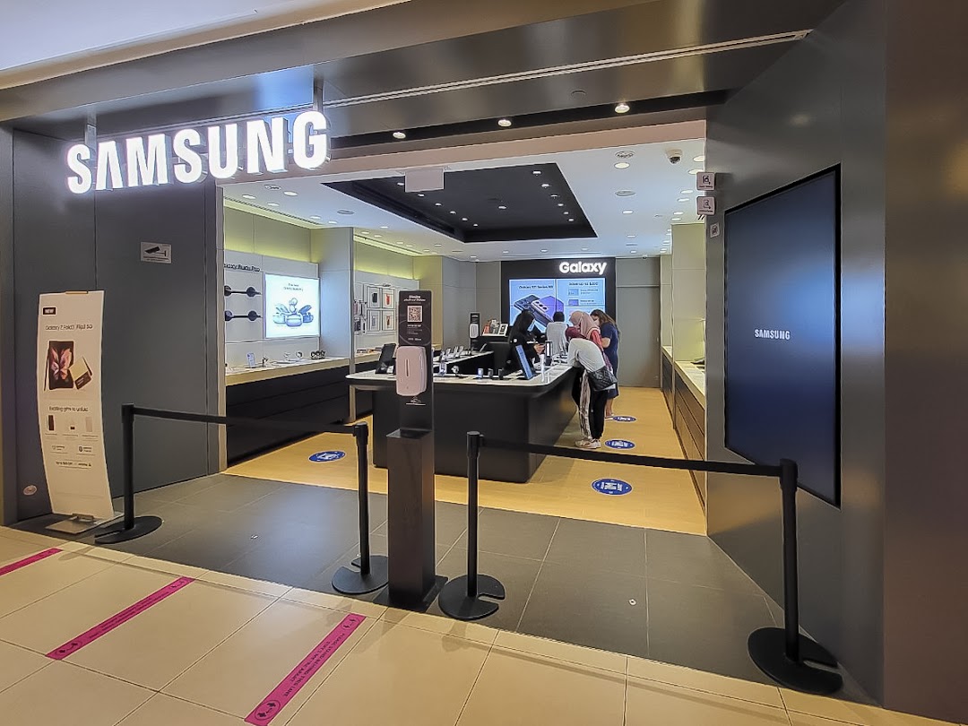 The entrance of a Samsung Experience Store, featuring its illuminated logo, interactive displays, and customers browsing devices.