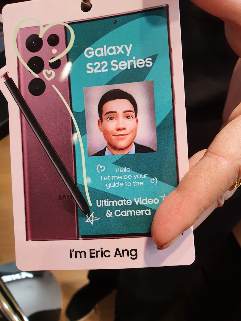 A person holds a promotional tag for the Samsung Galaxy S22 Series, featuring an avatar guide.
