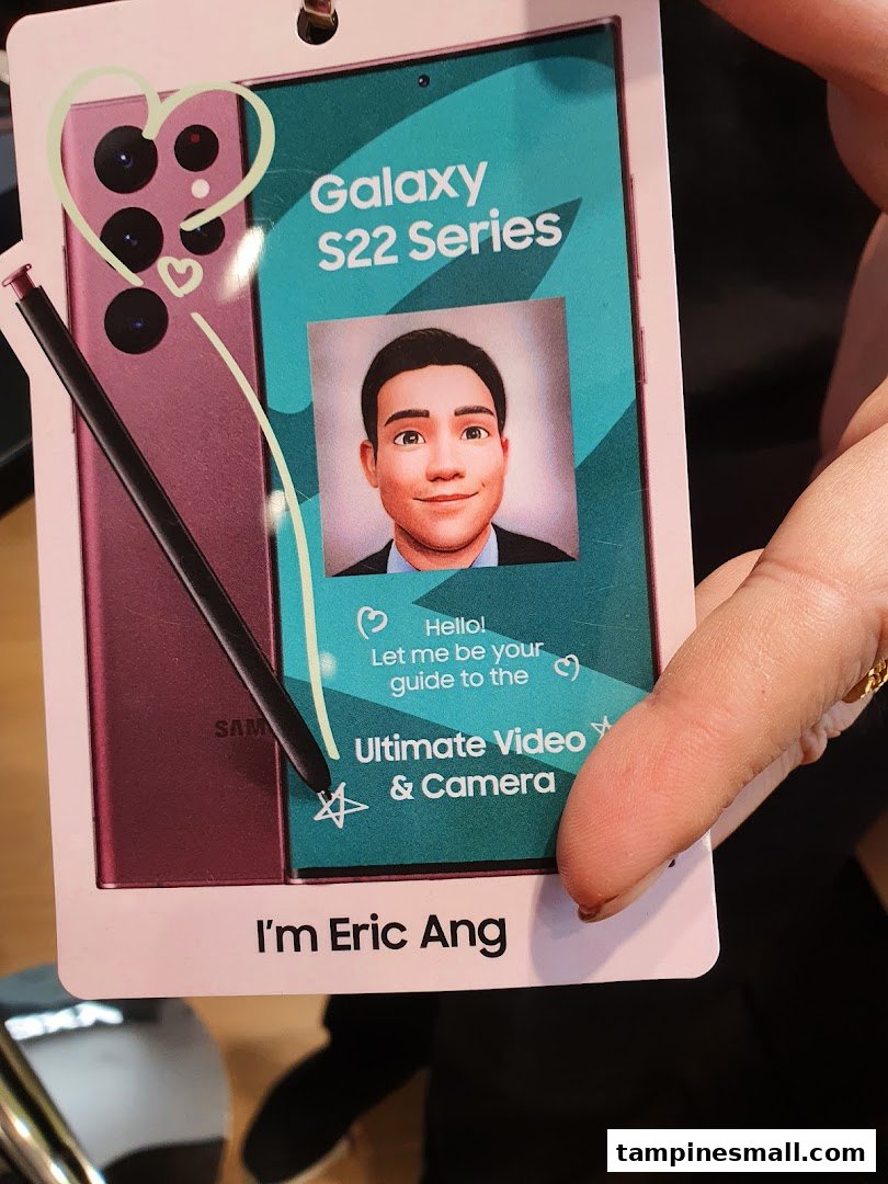 A person holds a promotional tag for the Samsung Galaxy S22 Series, featuring an avatar guide.