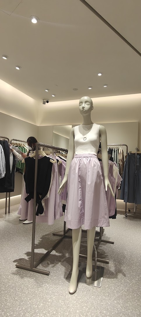 An interior view of SANS SANS clothing store, featuring a mannequin dressed in a white top and lavender skirt.