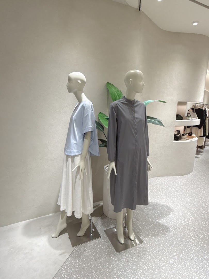 Two mannequins display minimalist fashion in a bright, modern retail store interior.