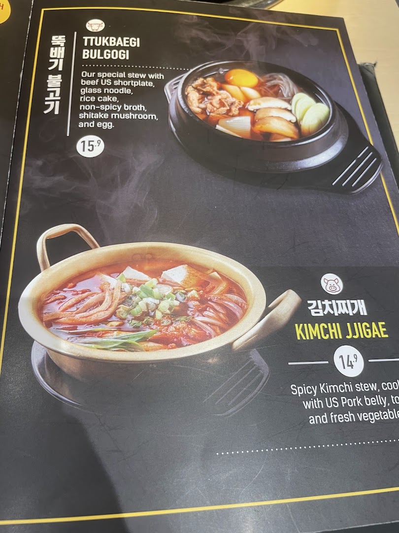 A close-up of a Korean restaurant menu featuring Ttukbaegi Bulgogi and Kimchi Jjigae.