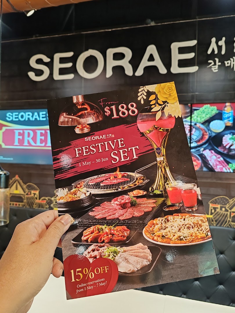 A hand holding a promotional flyer for Seorae Jib's Festive Set, with the restaurant interior in the background.