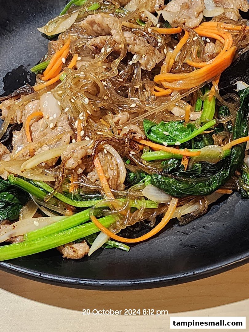 A close-up of a delicious Korean Japchae dish with glass noodles, beef, and vegetables.