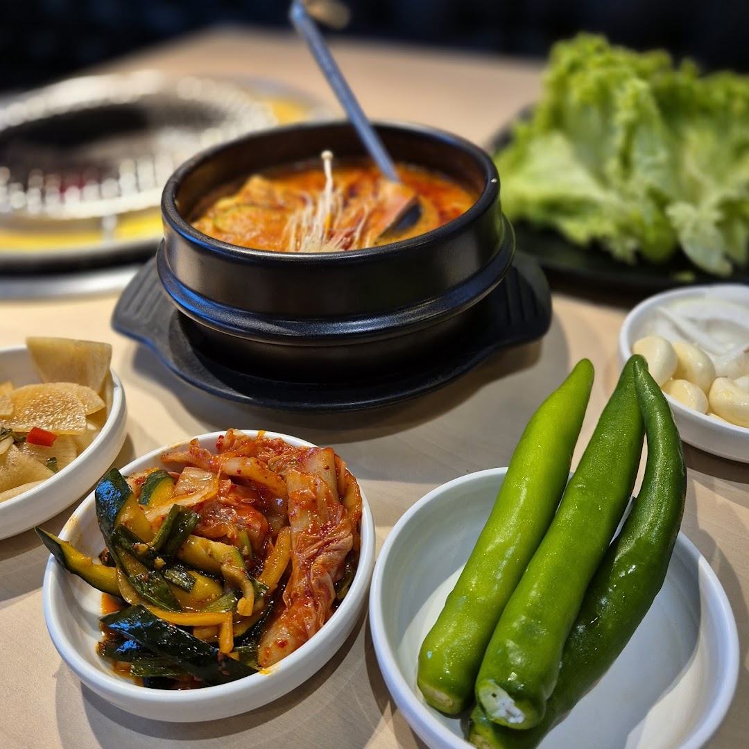 A close-up of a delicious Korean stew with an array of fresh banchan, including kimchi and green peppers.