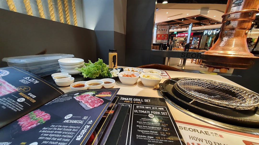 A table at Seorae Jib Korean BBQ, featuring open menus, side dishes, and a grill.