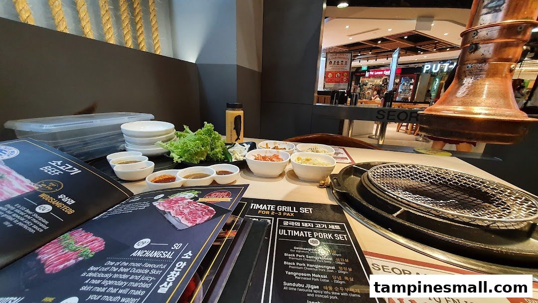 A table at Seorae Jib Korean BBQ, featuring open menus, side dishes, and a grill.