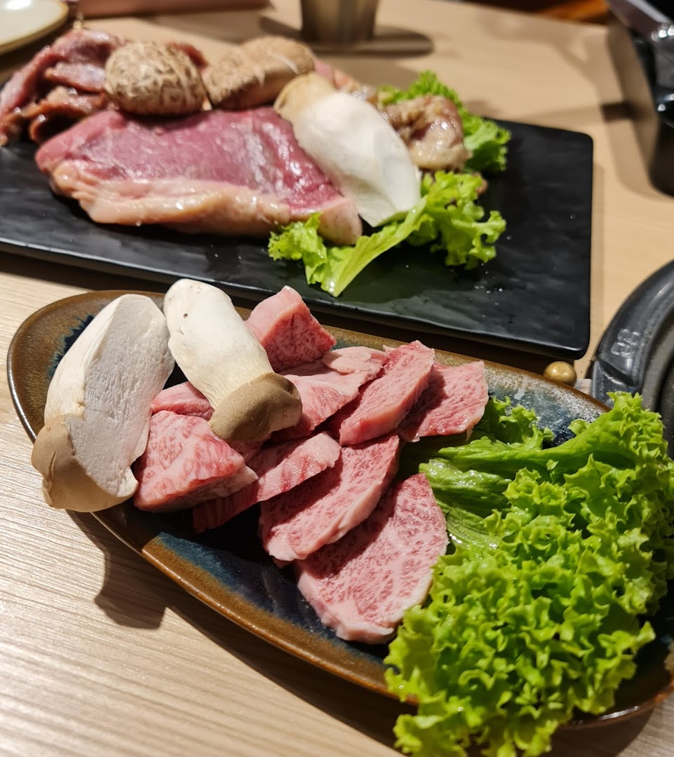Plates of raw marbled beef, mushrooms, and fresh lettuce, ready for grilling.