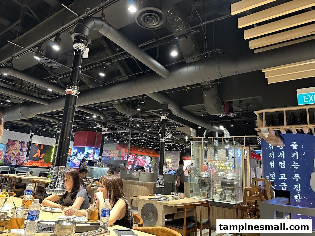 Interior view of a bustling Korean BBQ restaurant with diners and industrial-style decor.
