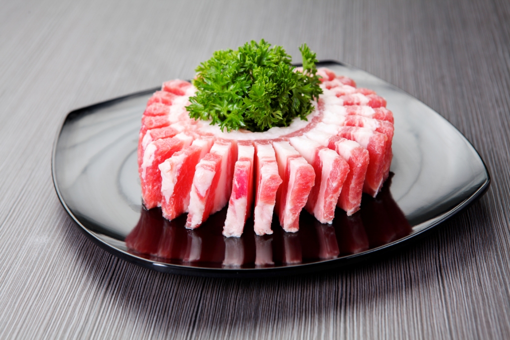 A plate of thinly sliced raw pork belly arranged in a circle with fresh green garnish.