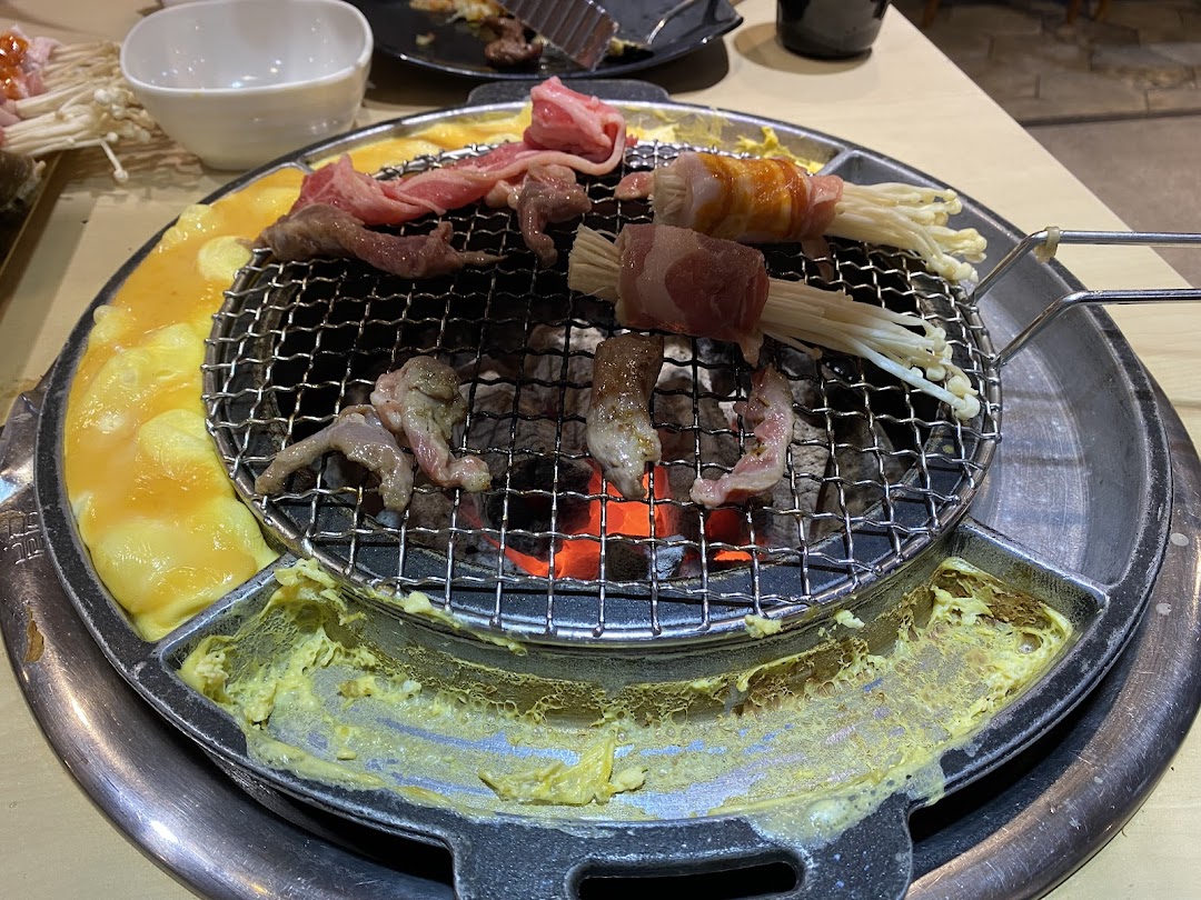 Close-up of various meats and enoki mushrooms grilling on a charcoal BBQ with an egg moat.