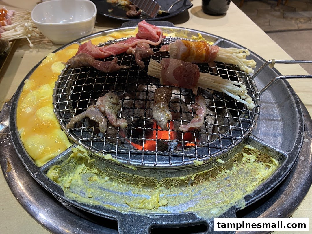 Close-up of various meats and enoki mushrooms grilling on a charcoal BBQ with an egg moat.