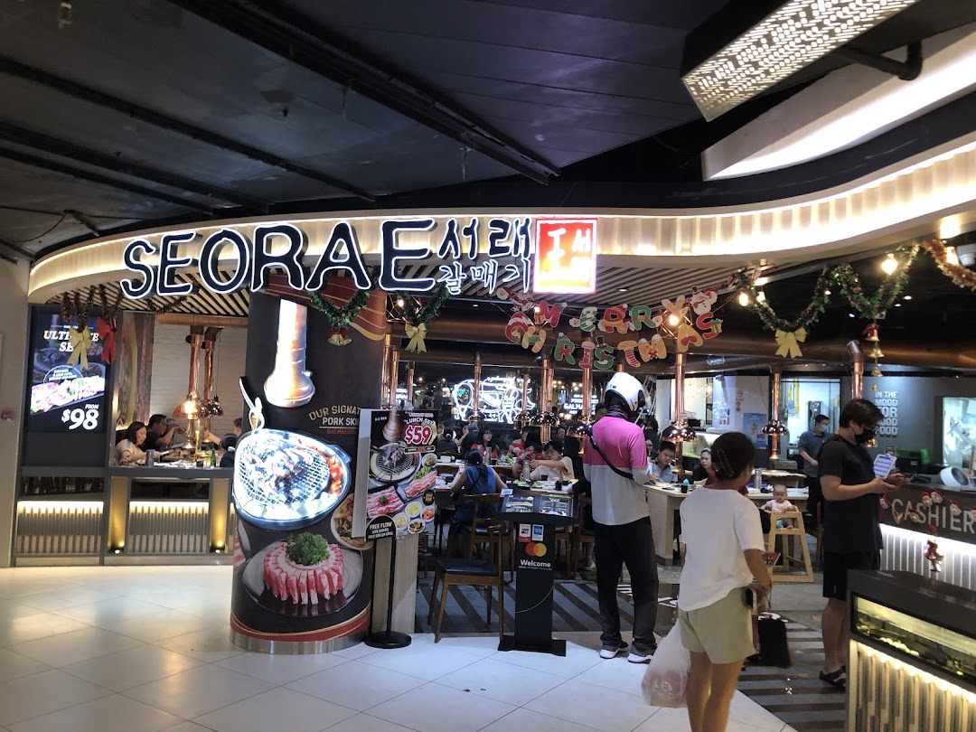 The brightly lit entrance of Seorae Jib, a Korean BBQ restaurant, with customers dining inside.