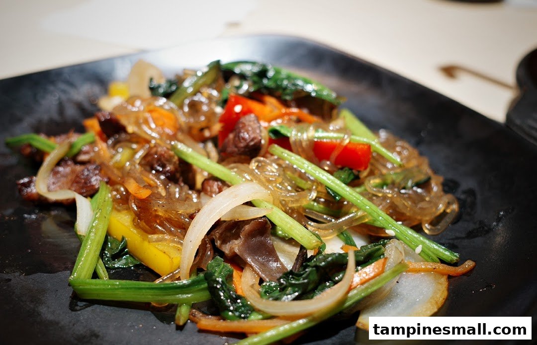 A vibrant plate of Korean Japchae with glass noodles, colorful vegetables, and savory meat.