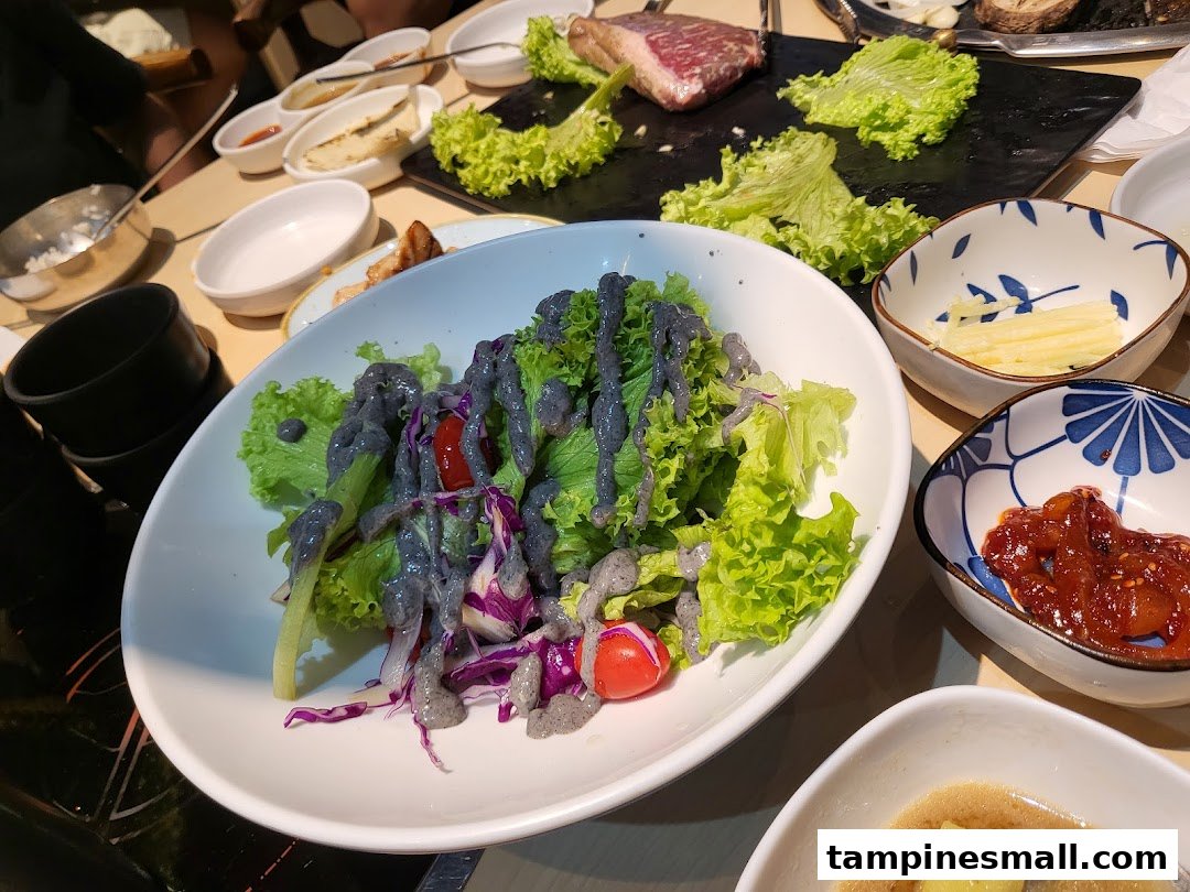 A vibrant table spread at Seorae Jib featuring fresh salad, banchan, and raw meat for grilling.