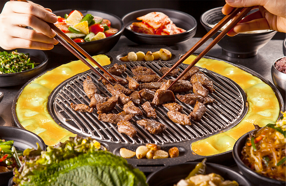 A close-up of Korean BBQ grilling meat and eggs, surrounded by various delicious side dishes.
