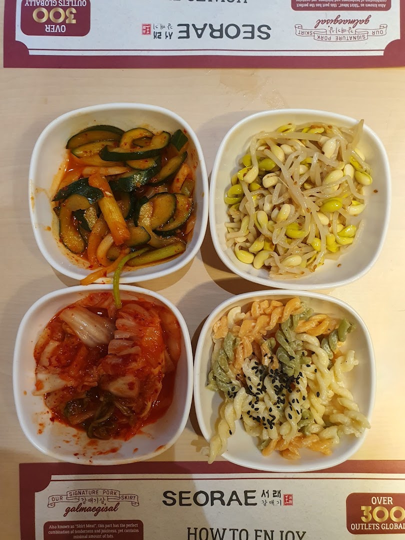 Four bowls of Korean side dishes, including kimchi and bean sprouts, on a table.