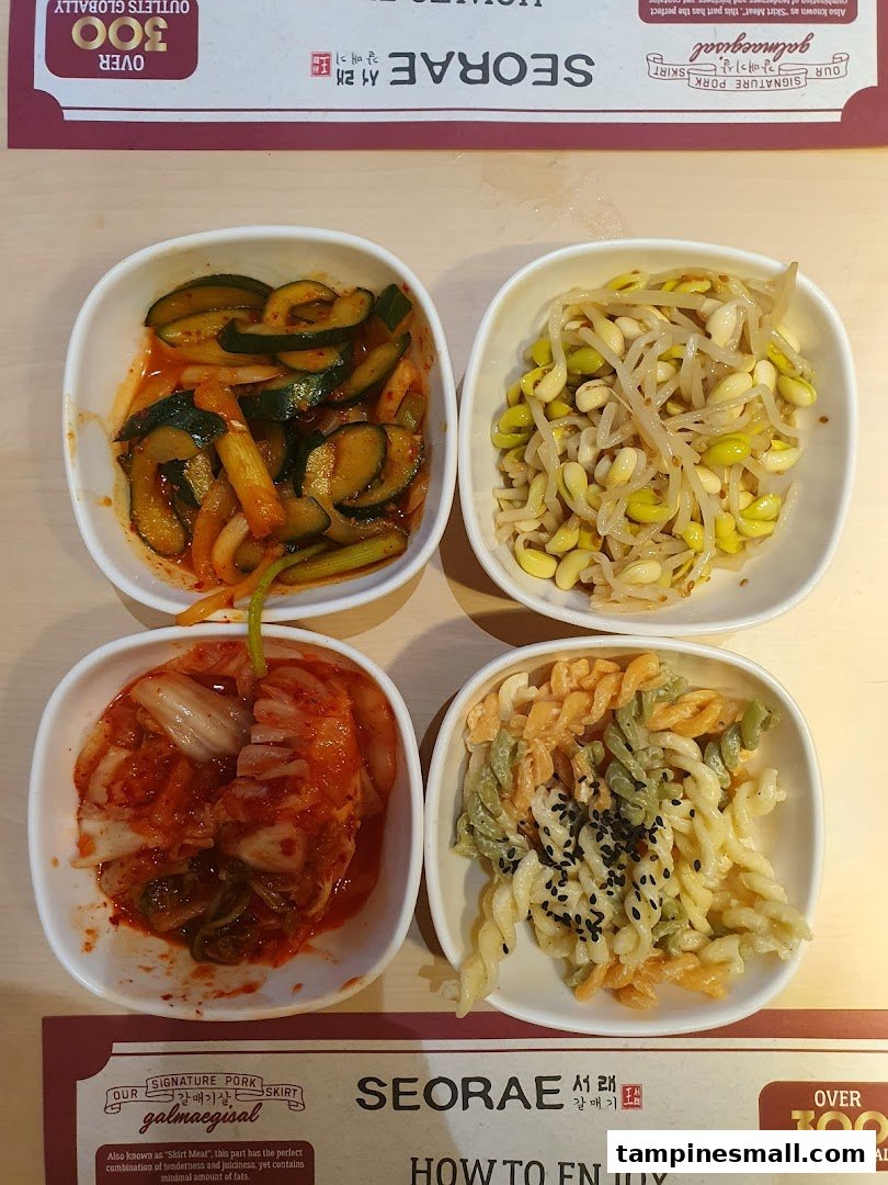 Four bowls of Korean side dishes, including kimchi and bean sprouts, on a table.