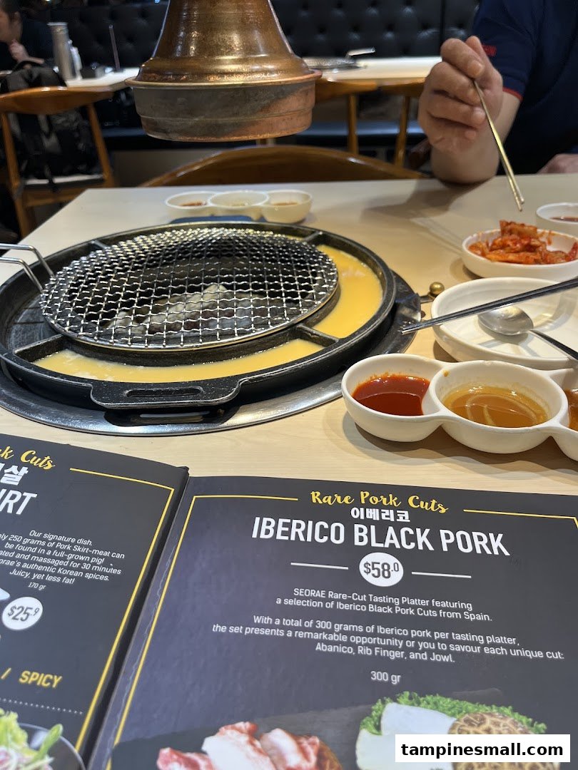 A Korean BBQ table with a grill, side dishes, and an open menu displaying premium pork cuts.
