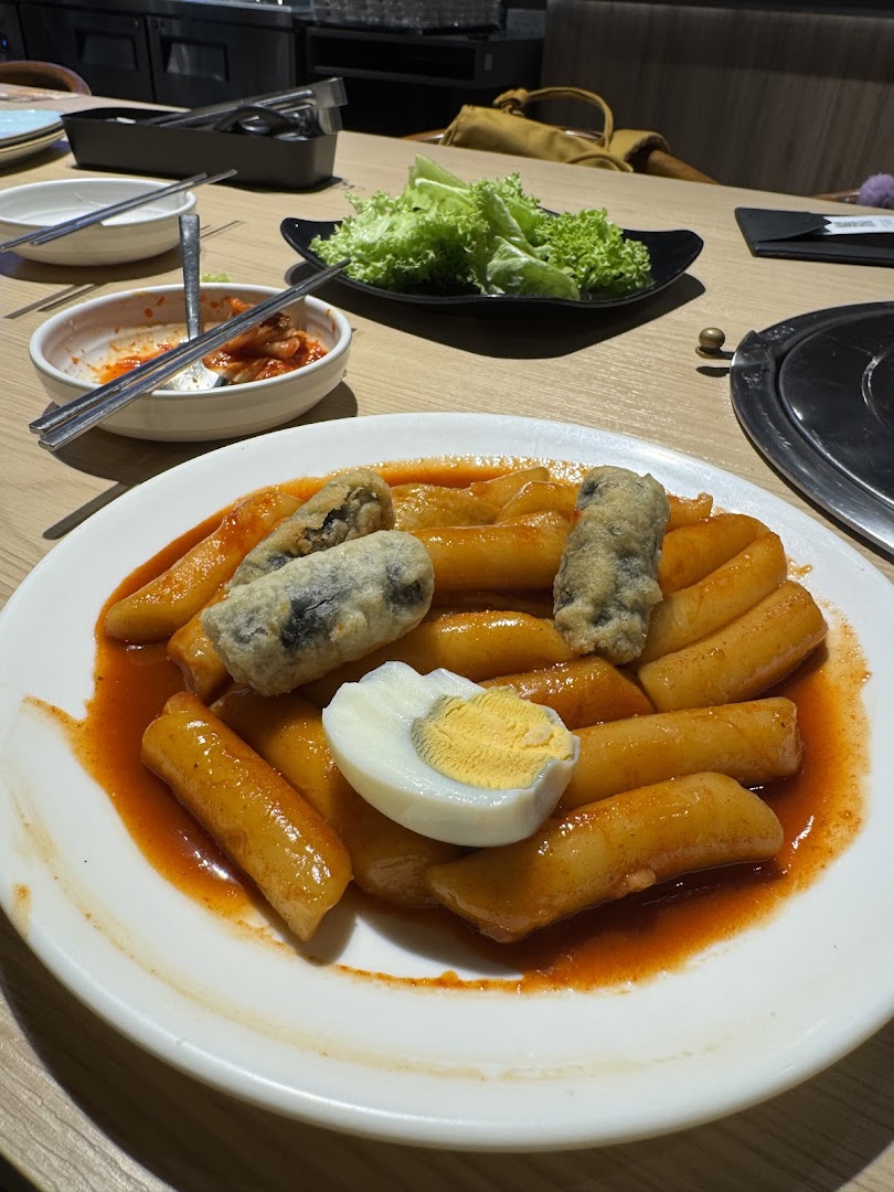 A close-up of a plate of spicy Tteokbokki with fried items and a boiled egg on a restaurant table.
