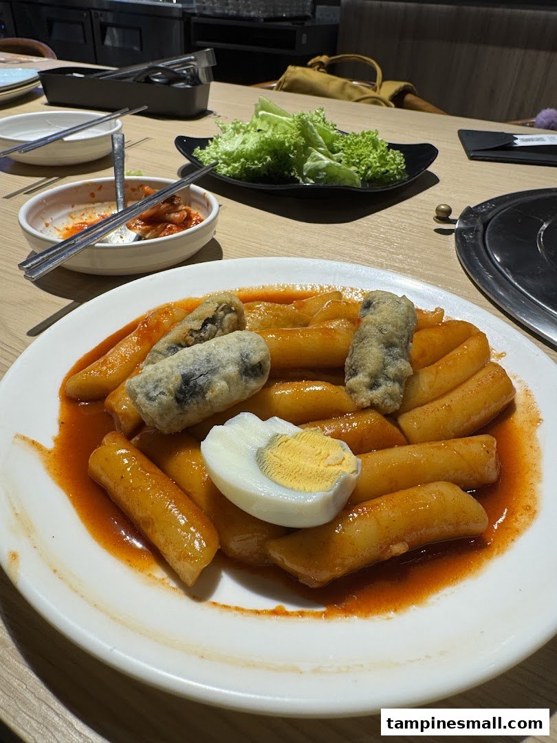 A close-up of a plate of spicy Tteokbokki with fried items and a boiled egg on a restaurant table.
