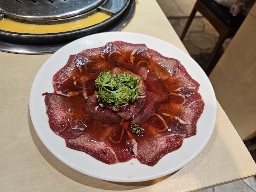 A plate of thinly sliced raw meat, possibly beef tongue, garnished with parsley, ready for grilling.
