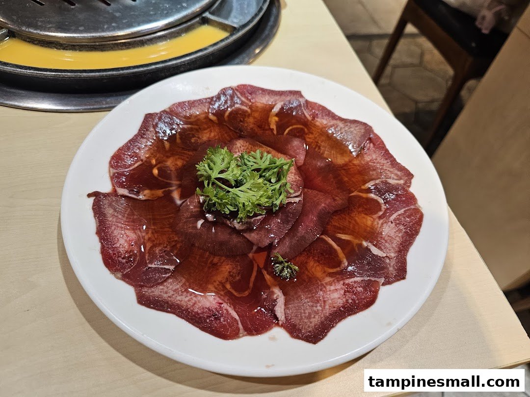 A plate of thinly sliced raw meat, possibly beef tongue, garnished with parsley, ready for grilling.