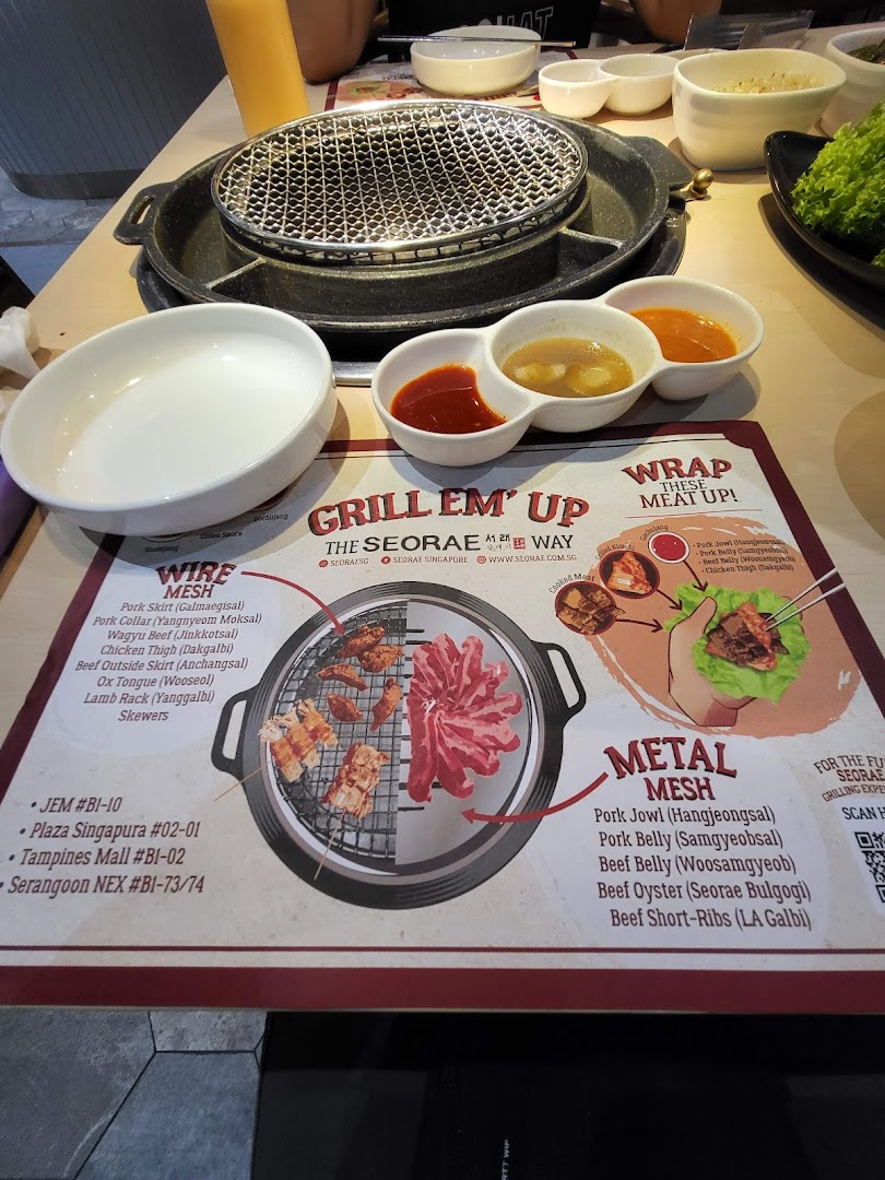 A Korean BBQ table setup featuring a grill, sauces, and a placemat detailing various meat cuts for grilling.