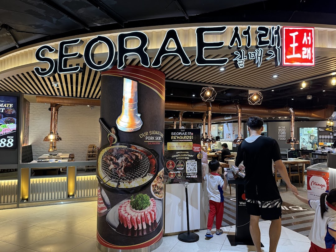 The inviting entrance of Seorae Jib, a Korean BBQ restaurant, featuring its prominent signage and promotional displays.