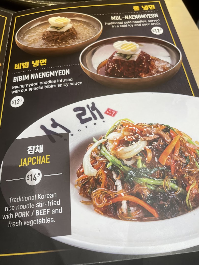 A close-up image of a menu displaying various Korean noodle and stir-fried dishes with prices.