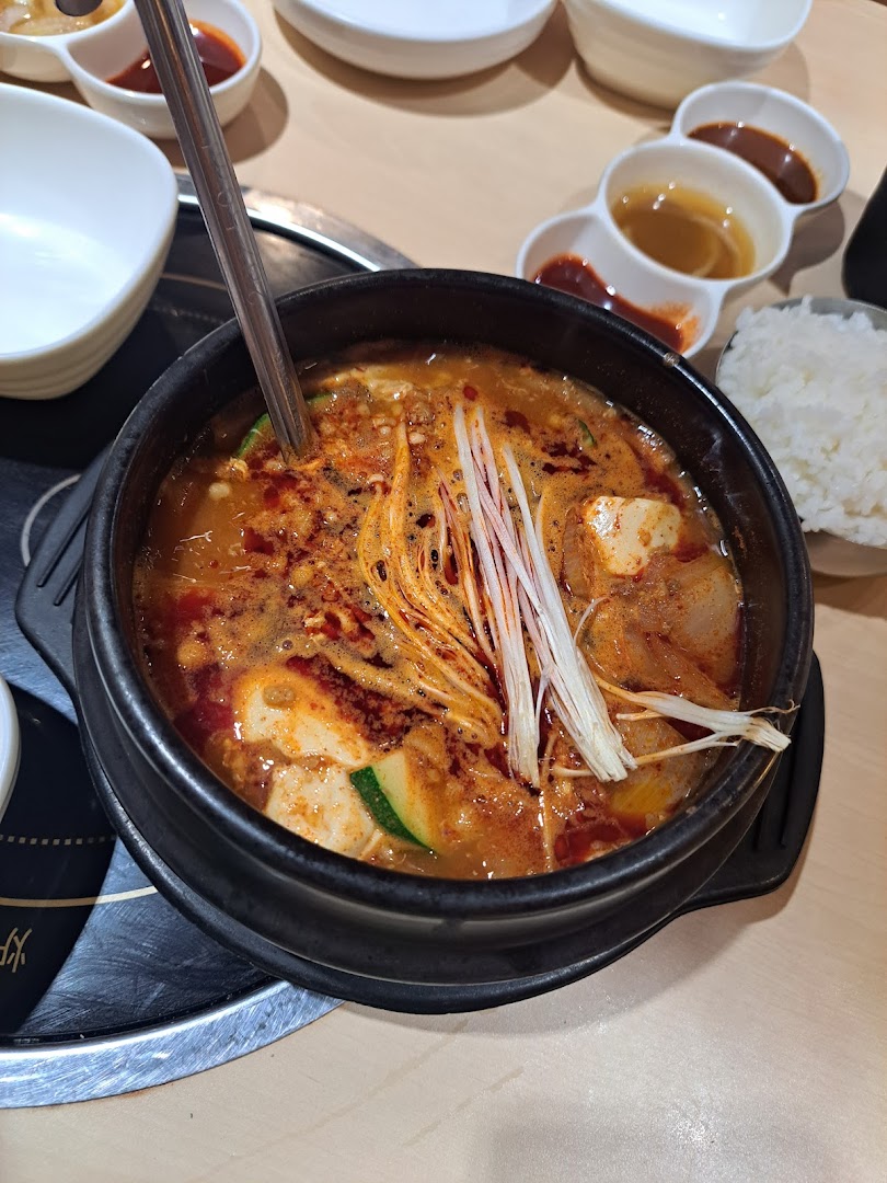 A close-up of a bubbling Korean hot pot with tofu, vegetables, and mushrooms, served with rice and side dishes.