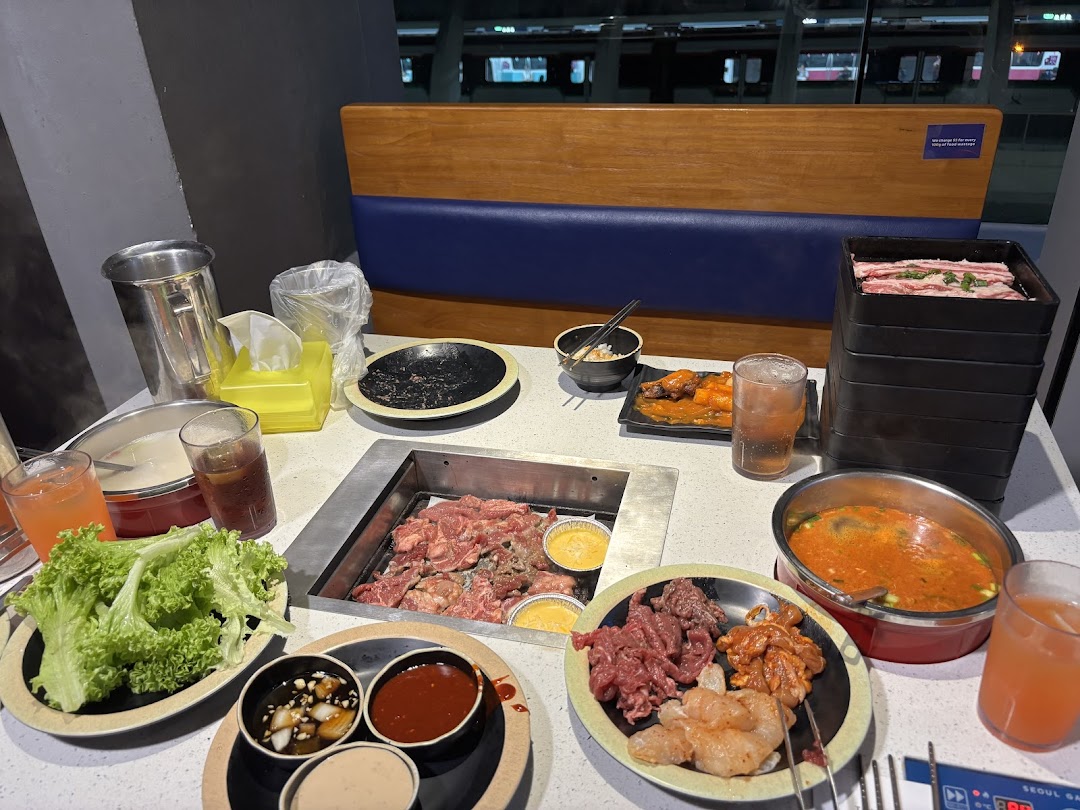 A dining table at Seoul Garden with a grill, raw meats, soup, and various Korean BBQ dishes.