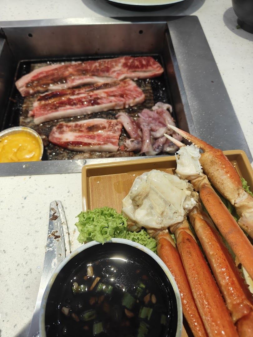A close-up of beef slices and squid grilling, with crab legs and dipping sauce on the side.