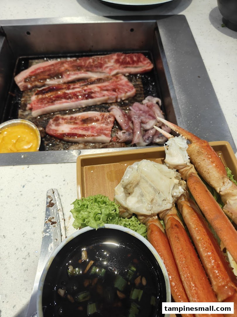 A close-up of beef slices and squid grilling, with crab legs and dipping sauce on the side.
